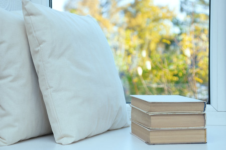 In the summer a white pillow and books stand on the windowsill by the window.の写真素材