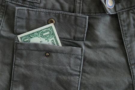 Dollar bill in a pocket of gray trousers close-up.
