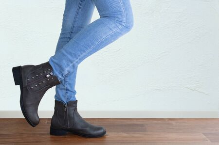 Legs of a girl in blue jeans and brown boots close-up. Against the background of a white wall.の写真素材