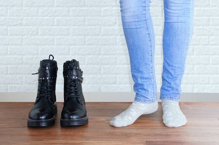 Legs of a girl in blue jeans and socks next to a pair of black boots. Against the background of a white brick wall.の写真素材