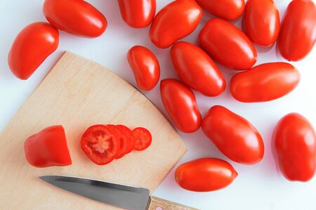 Red plum variety tomatoes on a wooden cutting board with a knife on a white background. View from above.の写真素材