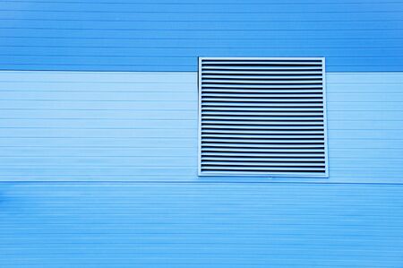 Close-up metal ventilation grill on the facade of a blue building.