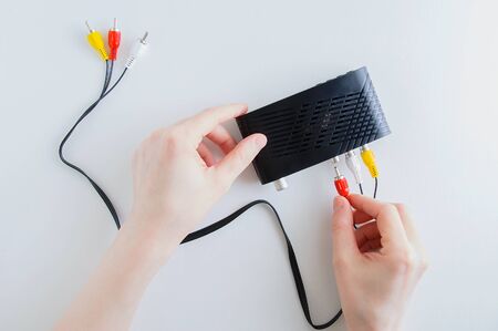 Caucasian woman connect an analog cable to the jack on a black digital television set-top box.