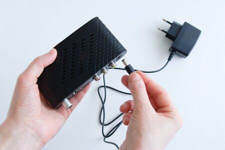 Caucasian woman connect power cable to jack on black digital set top box.