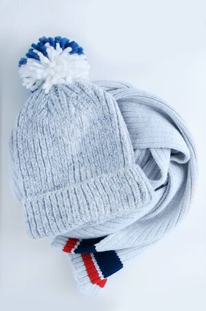 Woolen gray hat with a blue pompom and scarf on a white background.