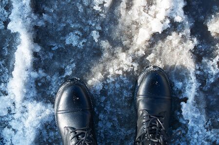 Feet in black boots in wet weather. Melting snow. View from above.の写真素材