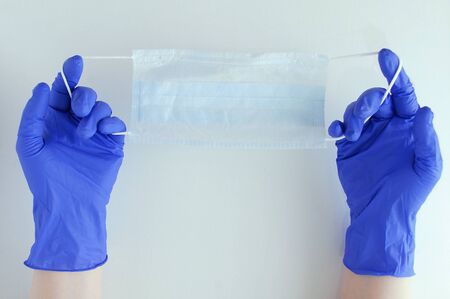 Caucasian girl in surgical gloves holds a protective face mask on a white background.の写真素材