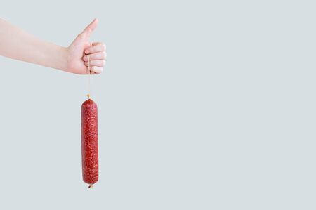 Smoked sausage in the hand of a caucasian woman. Gray isolate.の写真素材