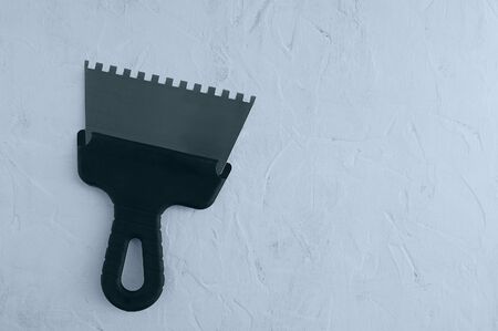 Metal notched construction spatula for tile adhesive with a black handle on a gray concrete background. View from above.の写真素材