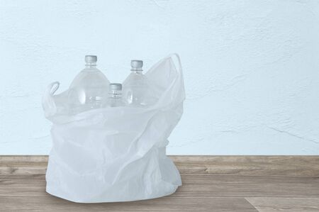 White plastic bag with garbage from plastic bottles on the floor in the room.