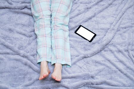 Legs of a girl in home clothes and a tablet computer on a gray plaid