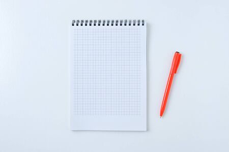 Notepad on a cell spring and an orange pen on a white background. View from above.