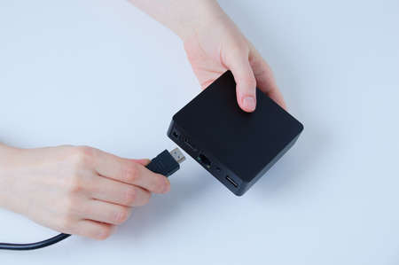 Hands of caucasian woman connects hdmi cable TV box to black box. White background.