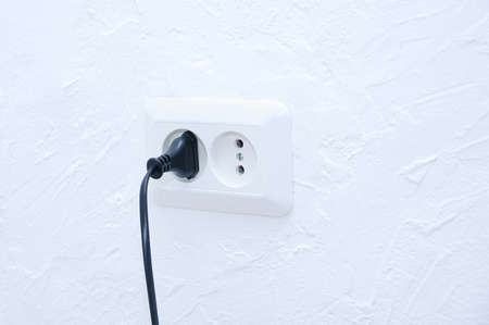 A black plug from an electrical appliance into a white electrical outlet.の写真素材