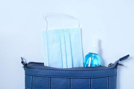 Open blue ladies bag with medical face mask and sanitizer in a bottle.