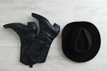 Black cowboy boots and black hat on a gray wooden background. View from above.