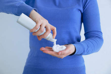 Caucasian woman in blue sweatshirt squeezes foam hair styling into her hand.の写真素材