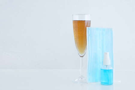 A glass of champagne, medical protective mask and hand sanitizer spray.