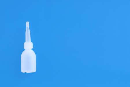 White plastic bottle with drops for nose and eyes close-up. Blue background.