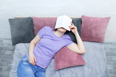 Caucasian young woman lying on the bed. The face is covered with a book. View from above.