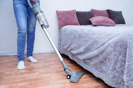 Handheld gray vacuum cleaner in the hand of a Caucasian woman in jeans. Vacuum the floor in the room.の写真素材