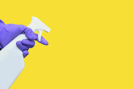 White bottle with a spray bottle in hand in a protective glove. Yellow isolate.の写真素材