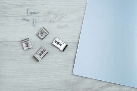 Metallic set for fixing a mirror with screws and a mirror on a white wooden background.