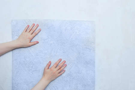 Caucasian woman applies a roll of paper wallpaper to the wall. Hands close up.