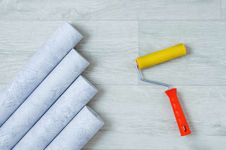 Gray textured wallpaper rolls and wallpaper roller on a white wooden background.の写真素材