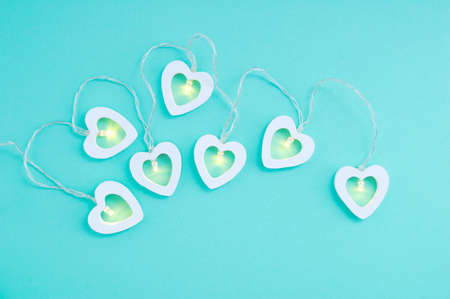 Electric white garland with glowing lights in the form of hearts on a turquoise background.の写真素材