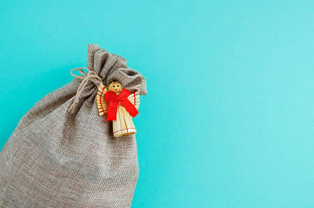 Brown canvas bag with ties and a straw angel with a red bow close-up on a turquoise background.の写真素材