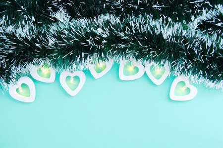 Electric white garland with glowing lights in the form of hearts and Christmas tinsel on a turquoise background. Place for your text.の写真素材