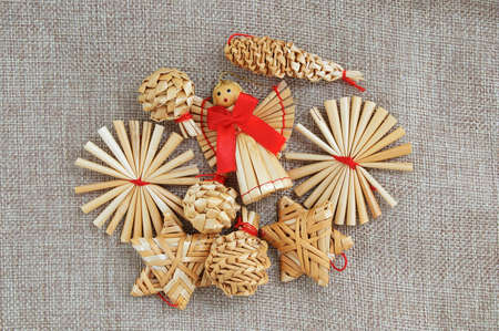 A straw angel with a red bow and Christmas decoration made of straw on a brown canvas fabric.