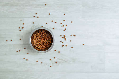 Scattered dry dog food in a metal bowl on a wooden white floor.の写真素材