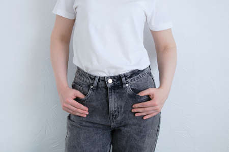 Caucasian woman in gray jeans and a white T-shirt on the background of a white wall.の写真素材