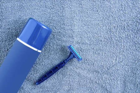 A blue razor and shaving foam in a cylinder against the background of a gray terry towel.