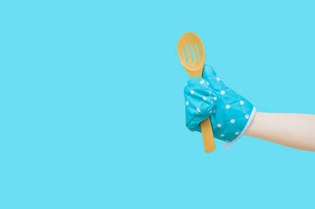 Wooden spoon and oven mitt in the hand of a Caucasian woman. Turquoise background isolate.
