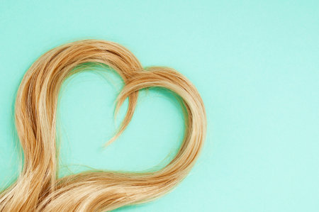 Blonde strands of hair in the shape of a heart. green background.の写真素材