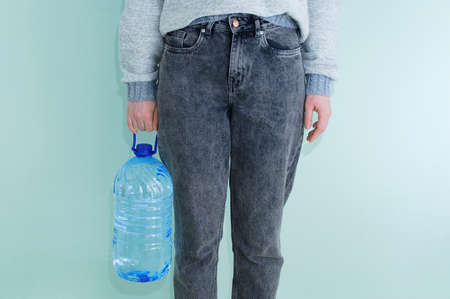 Caucasian woman in jeans with a large bottle of drinking water in her hand.