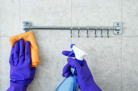 Rag and spray for cleaning in hands in protective gloves. Cleaning tiles and towel rails in the...