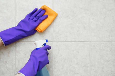 Rag and hand cleaning spray while wearing protective gloves. Washing tiles in the bathroom.の写真素材