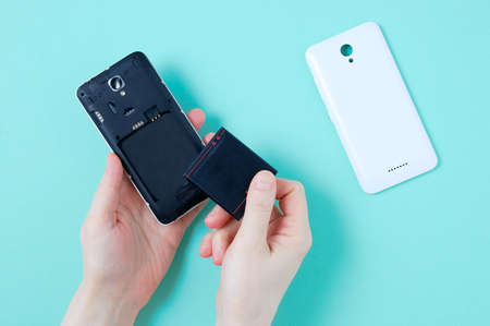 Removable battery smartphone in caucasian woman's hand. Turquoise background.の写真素材