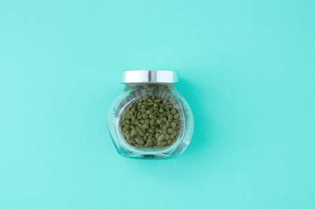 Green tea in a glass jar with a lid. Turquoise background.