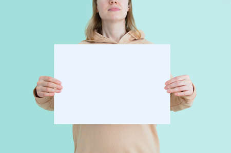 Young caucasian woman with white empty sheet of paper in her hands. Place for text. Turquoise...