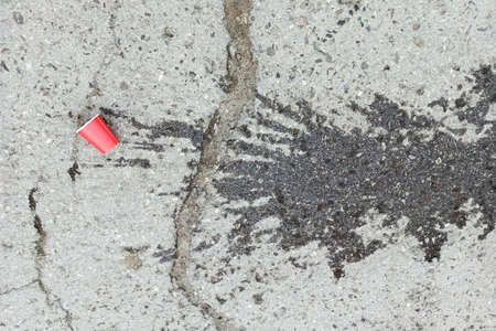 Paper glass lying on the pavement. spilled coffee. Crack in the sidewalk.