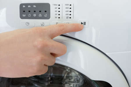 Presses the start button with his finger on the washing machine close-up.の写真素材