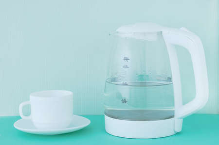 White glass teapot with hot water and drops of condensate and a cup and saucer. green background.の写真素材