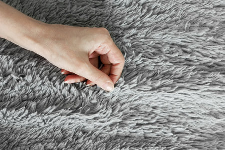 The hand of a Caucasian woman on the background of a gray fur plaid. Check the softness of the...