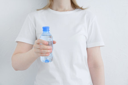 A bottle of drinking water in the hand of a caucasian woman. white background.の写真素材