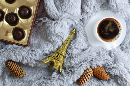 Christmas still life. A cup of coffee, chocolates in a box, a figure of the Eiffel Tower and cones on a gray fur plaid.の写真素材